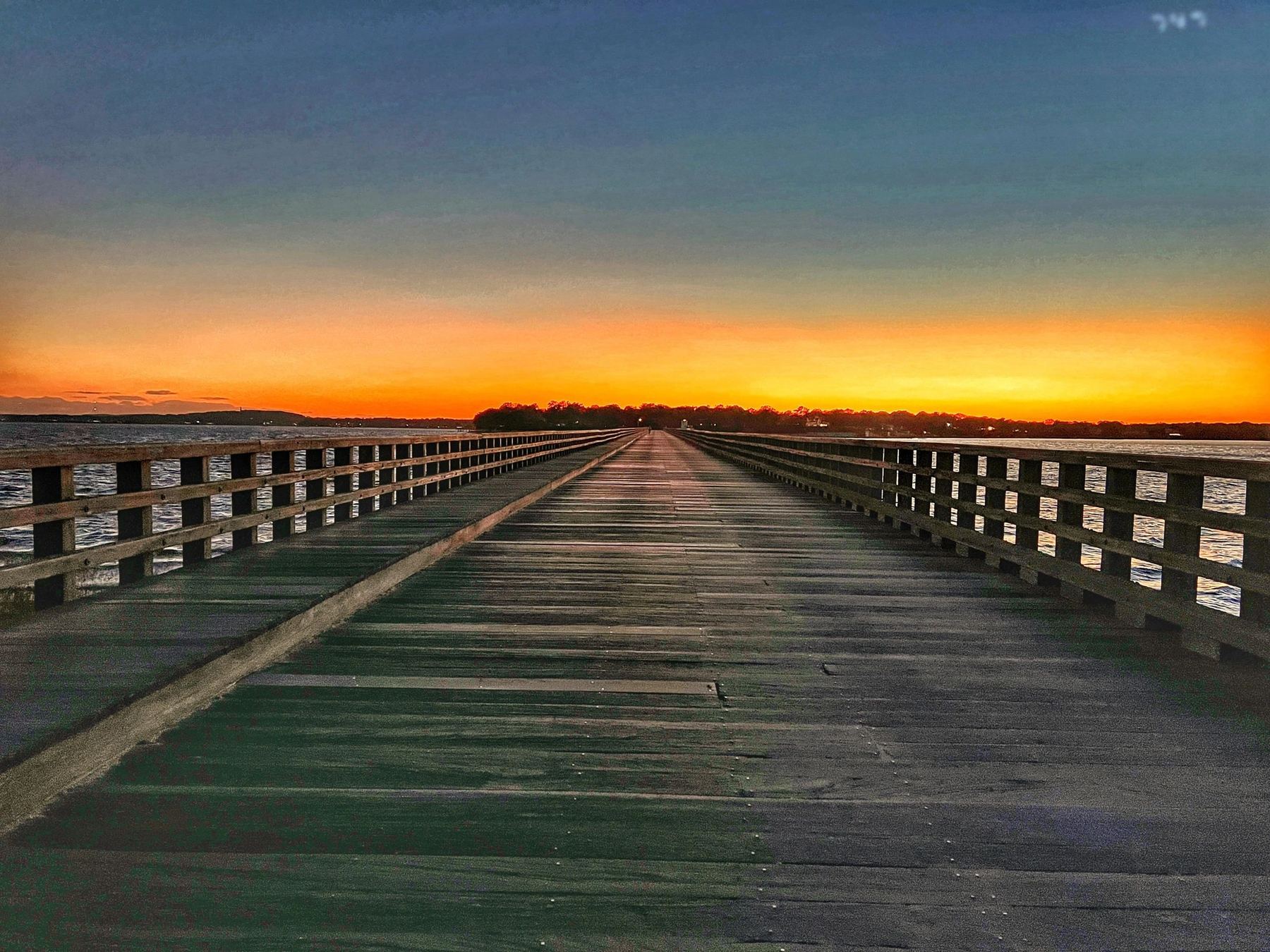 Powder Point Bridge in Duxbury running out over the water toward an orange sunset