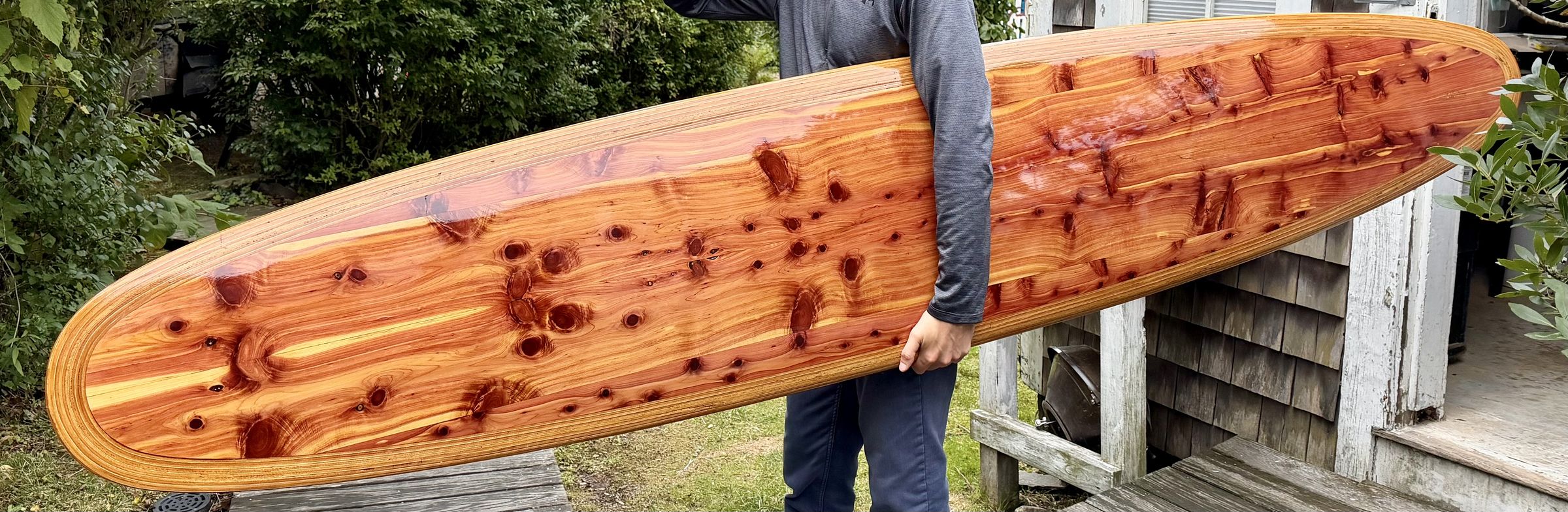 A finished nine-foot hollow cedar surfboard, carried under one arm