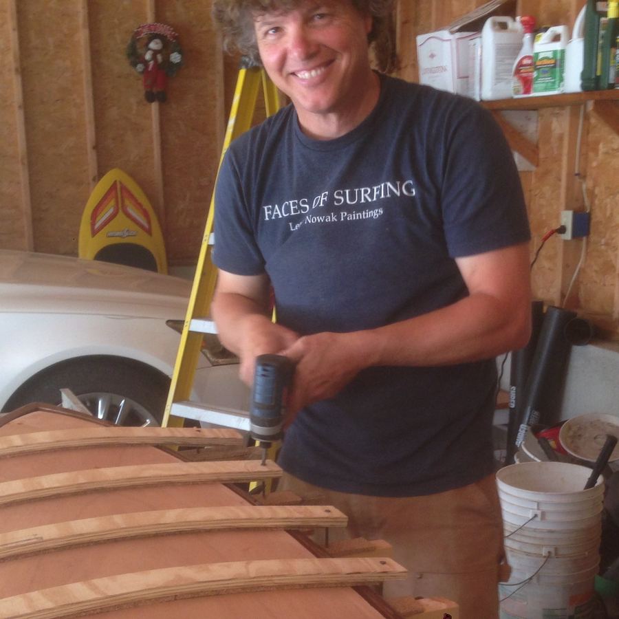 Rich Blundell smiling in his shop, working on a wooden surfboard frame