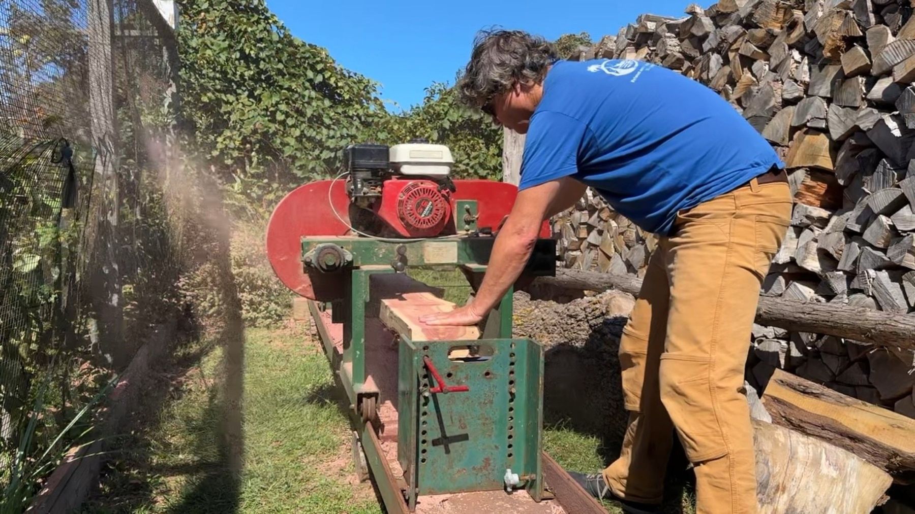 Two people milling a log on the ground with a portable chainsaw mill