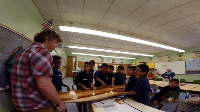 Rich with a wooden surfboard in front of a class of students