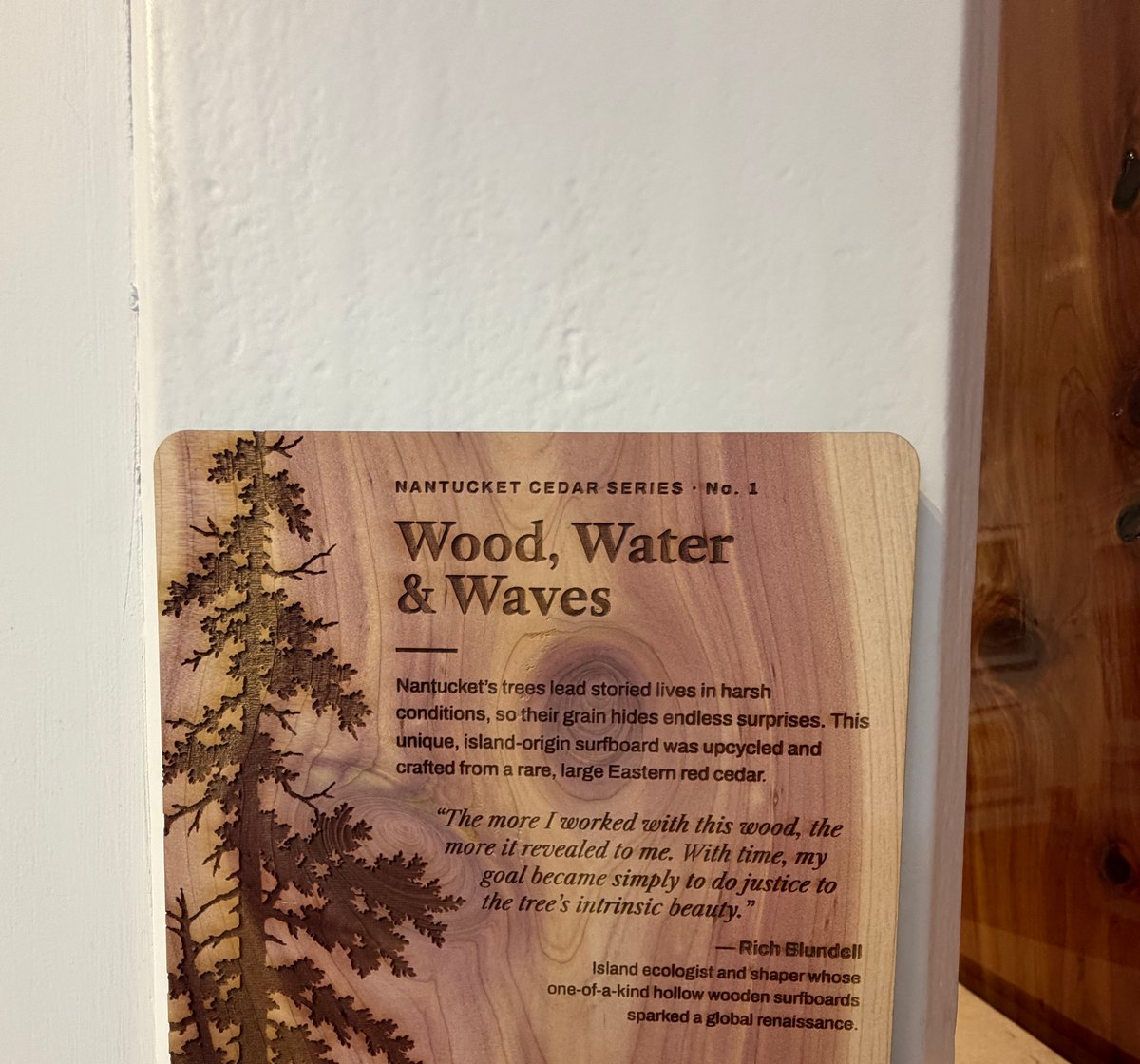 The gallery placard, laser-engraved on cedar: Nantucket Cedar Series No. 1, Wood, Water & Waves, with a description of the board and a quote from Rich Blundell