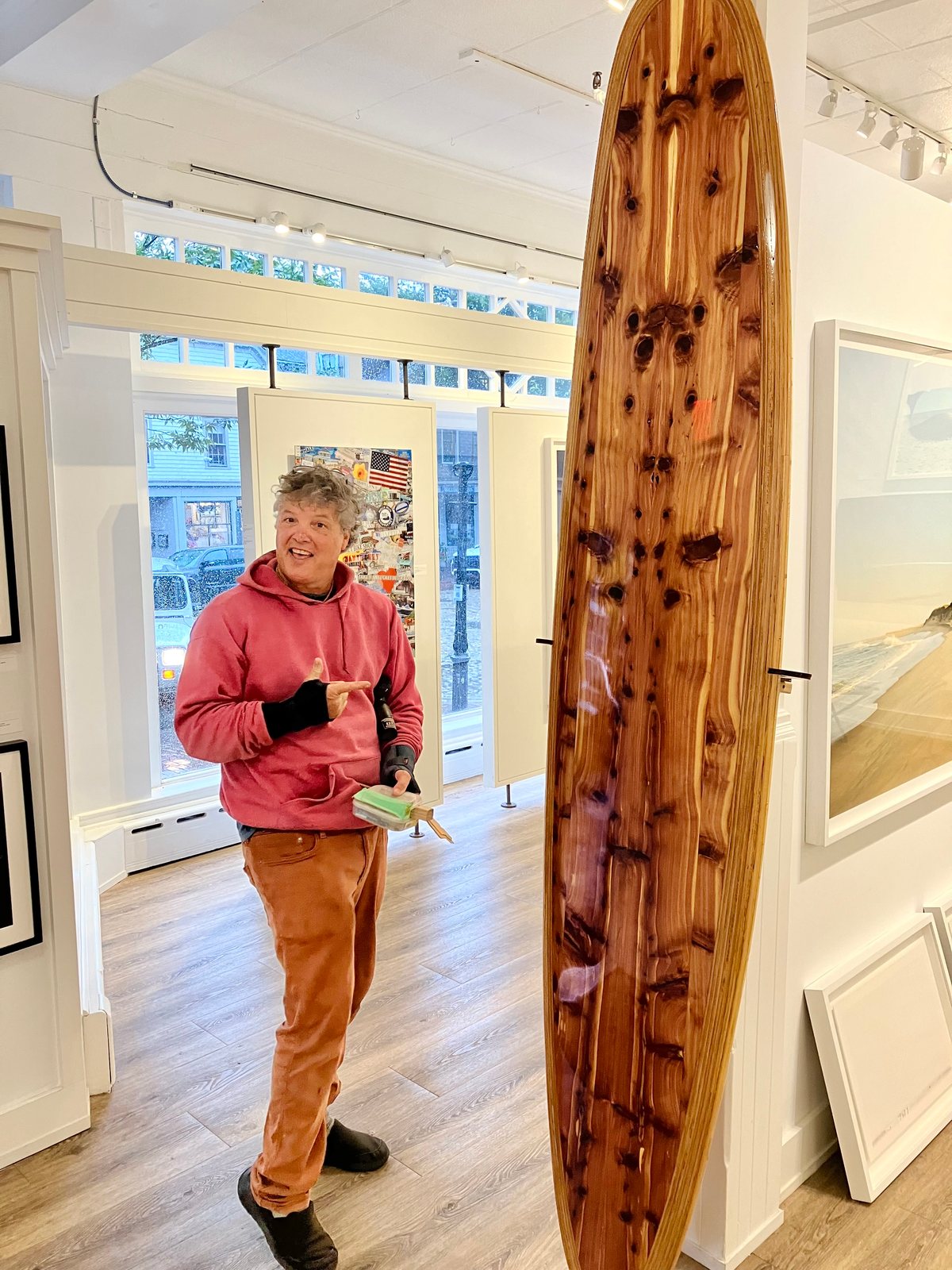 Rich standing beside the finished cedar board on its stand in a gallery hung with framed pictures
