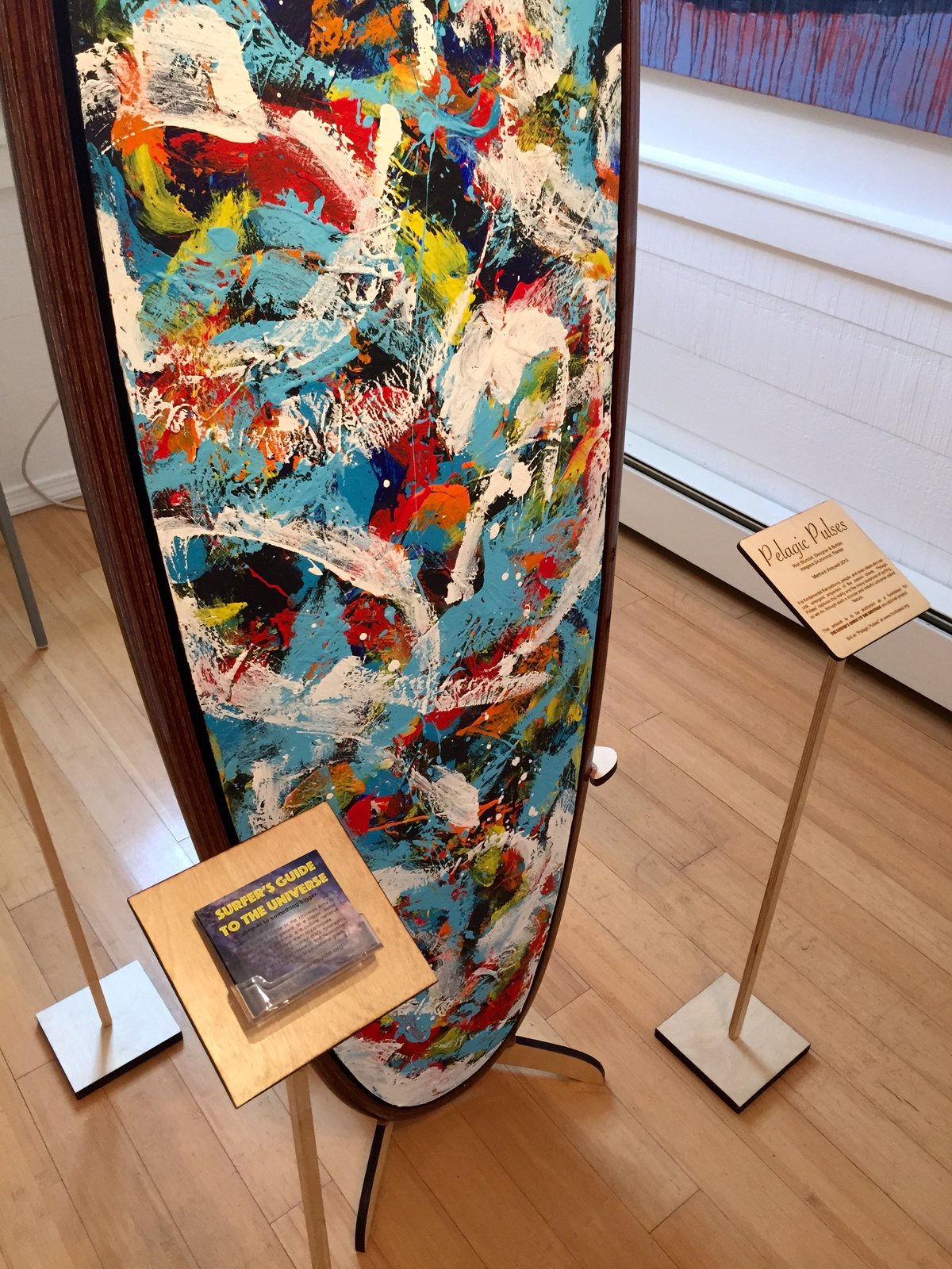 A painted surfboard on its display stand beside matching custom sign stands